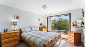 Une chambre à coucher comprenant un lit, une commode en bois, des tables de chevet, une fenêtre avec vue et des éléments de décoration fixés au mur.