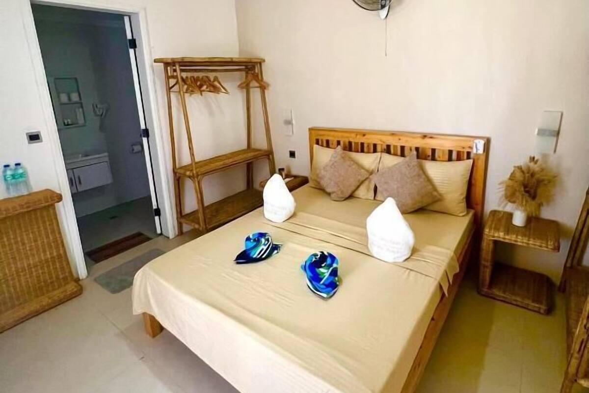 Ein Schlafzimmer mit Bett, Nachttisch, Wandventilator und einer Tür zu einem Badezimmer.