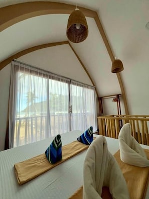 Una habitación con techo abovedado, una cama con almohadas, una lámpara colgante y una ventana con cortinas.