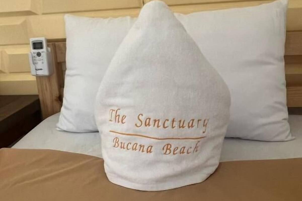 Ein Bett mit einem Kopfkissen, auf dem 'The Sanctuary Bucana Beach' steht.