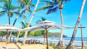Uma praia com cadeiras de praia brancas e guarda-sóis, palmeiras e vista para o oceano.