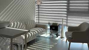 Ein modernes Wohnzimmer mit einer Couch, Sesseln, einem Glastisch und einer Stehlampe.