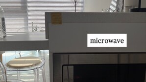 Eine Küche mit einer Mikrowelle, einem Glastisch und einem Stuhl.