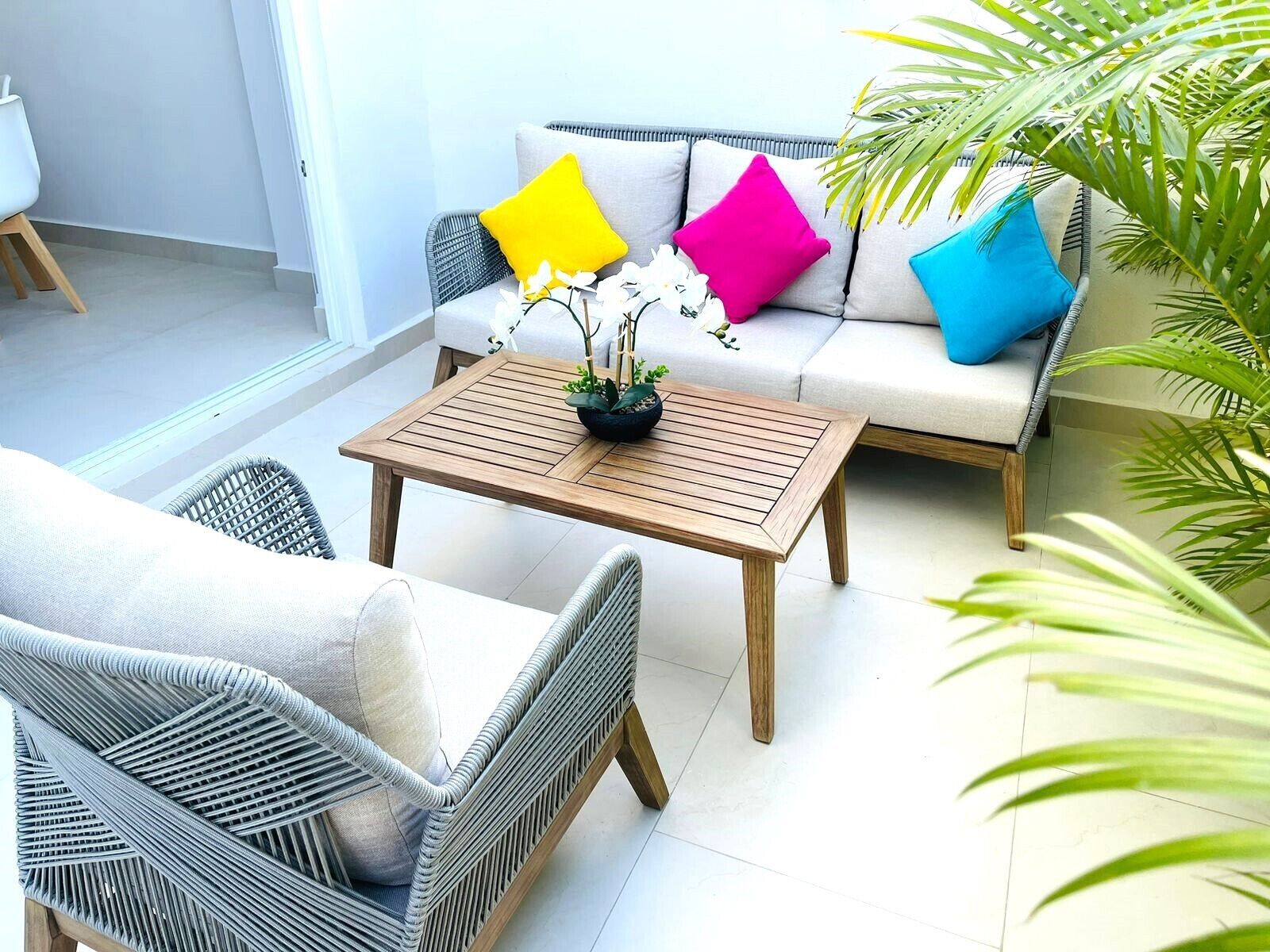 Uma área de estar moderna ao ar livre, com móveis de vime, mesa de madeira e almofadas coloridas.