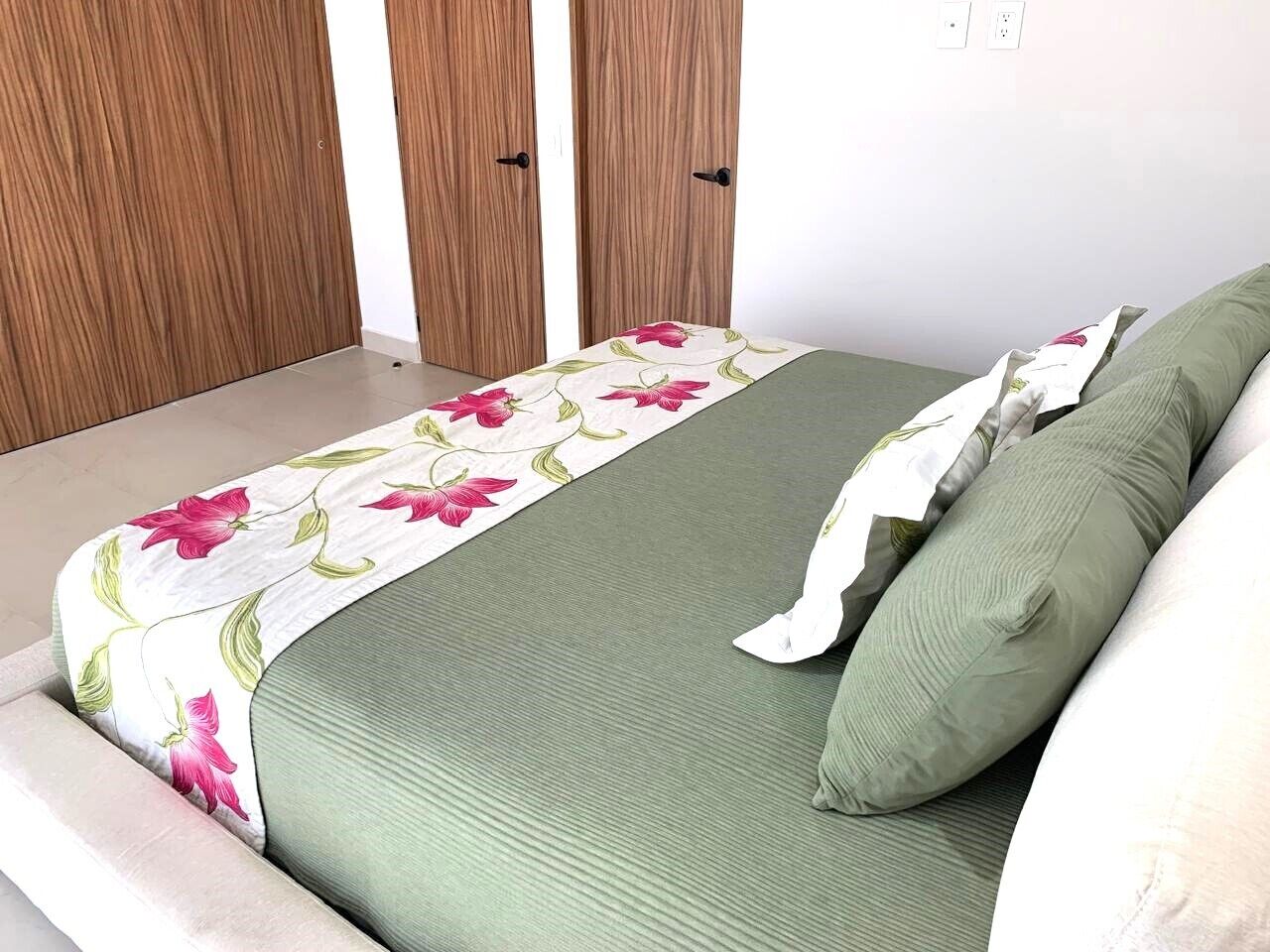 Een slaapkamer met een bed, groen beddengoed, een plaid met bloemenprint en houten deuren.