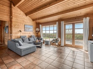 Ein Holzblockhaus-Innenraum mit einem grauen Ecksofa, einem runden Couchtisch und einem Schaukelstuhl.