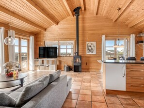 Ein modernes Blockhaus-Interieur mit Wohnbereich, Fernseher, Kamin, Küche und großen Fenstern.