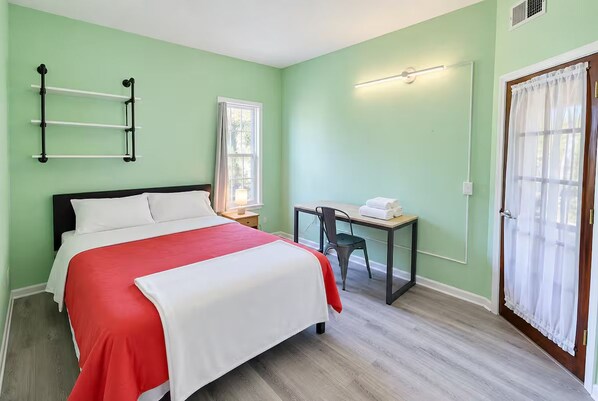 A bedroom with a bed, a desk, and a chair. There is a window with curtains and a door with a curtain.