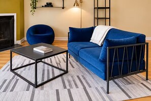 A living room with a blue sofa, a black coffee table, a blue armchair, a fireplace, and a floor lamp.