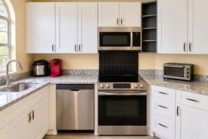 A modern kitchen with white cabinets, stainless steel appliances, a dishwasher, a stove, a microwave, and a toaster.