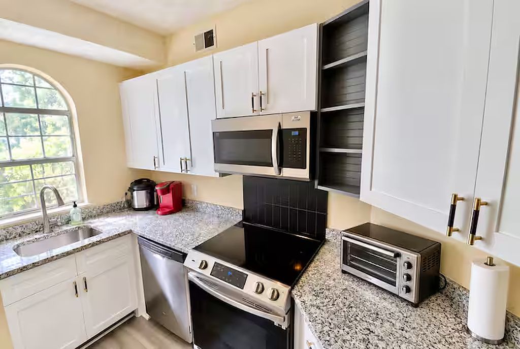 A kitchen with white cabinets, a microwave, a stove, a toaster, and a sink.
