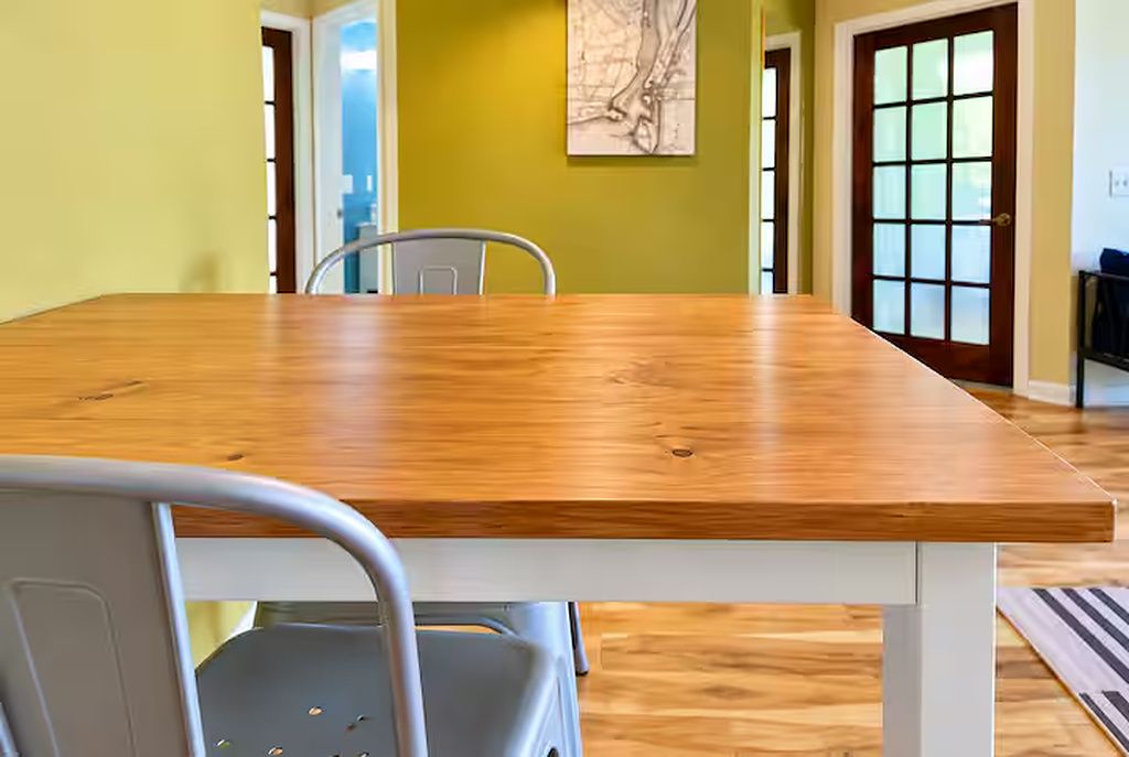 Uma sala de jantar com mesa de madeira e cadeiras de metal, uma obra de arte com mapa na parede e uma porta com painéis de vidro fosco.
