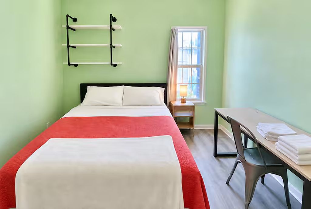 Ein Zimmer mit einem Bett, einem Schreibtisch, einem Stuhl, einem Fenster mit Vorhängen und einem fest montierten Handtuchhalter.