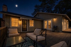 Ein Haus mit Terrasse, zwei Sofas, einem Grill und dem Mond am Himmel.