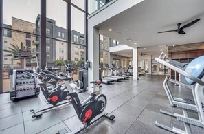 A gym with various exercise machines, large windows, and a modern interior design. - Cozy 1-bedroom apartment in fabulous Addison (Addison)