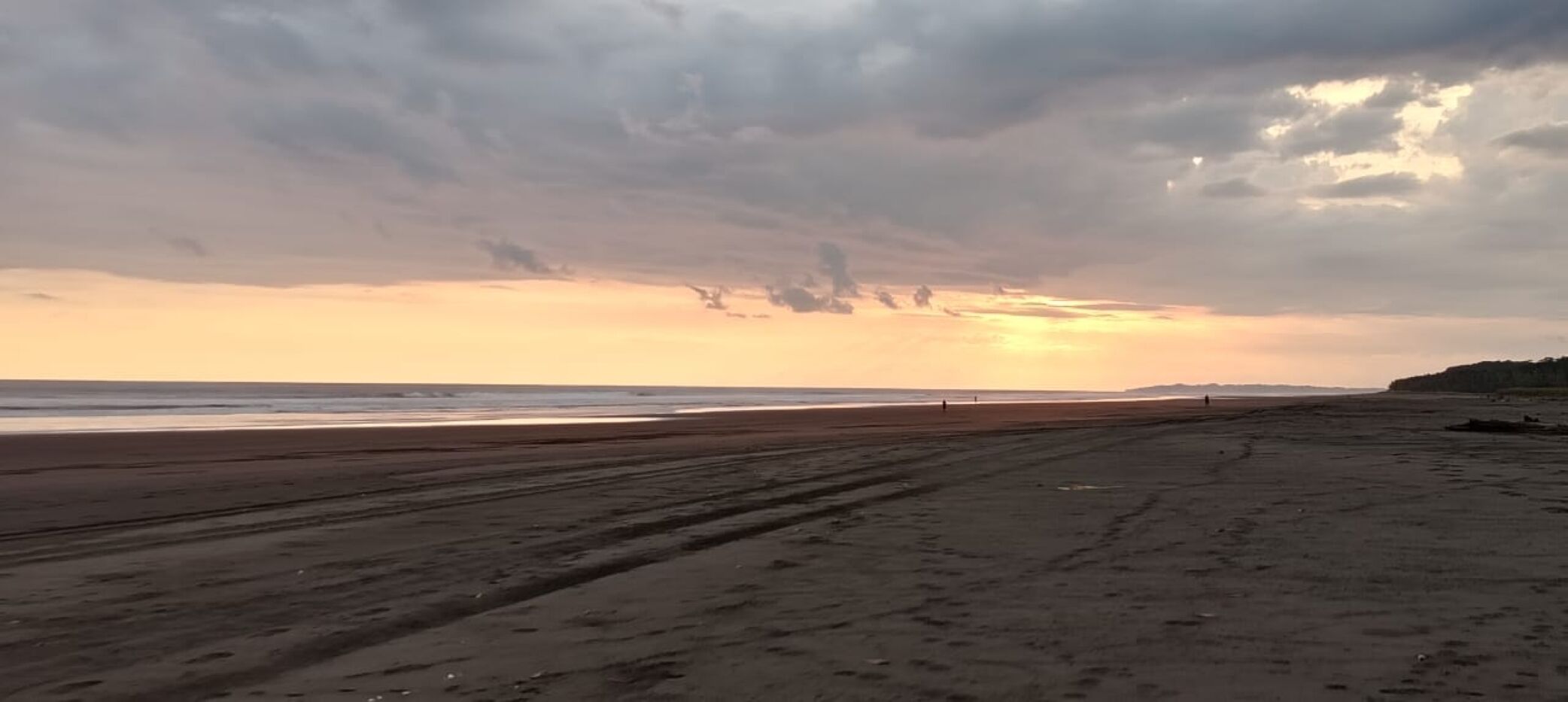 En strand med et stort sandområde og en fjerne havudsigt under en overskyet himmel.