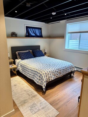 Une chambre à coucher comprenant un lit, des tables de chevet, une fenêtre et un plafond avec des poutres apparentes.