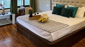 A hotel room with a bed, a desk, a chair, a ceiling fan, and a window with curtains. - Dhauladhar View Village Resort (Dharamshala)