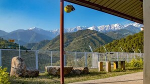 A covered outdoor area with a view of snow-capped mountains, a metal fence, and a bench. - Dhauladhar View Village Resort (Dharamshala)
