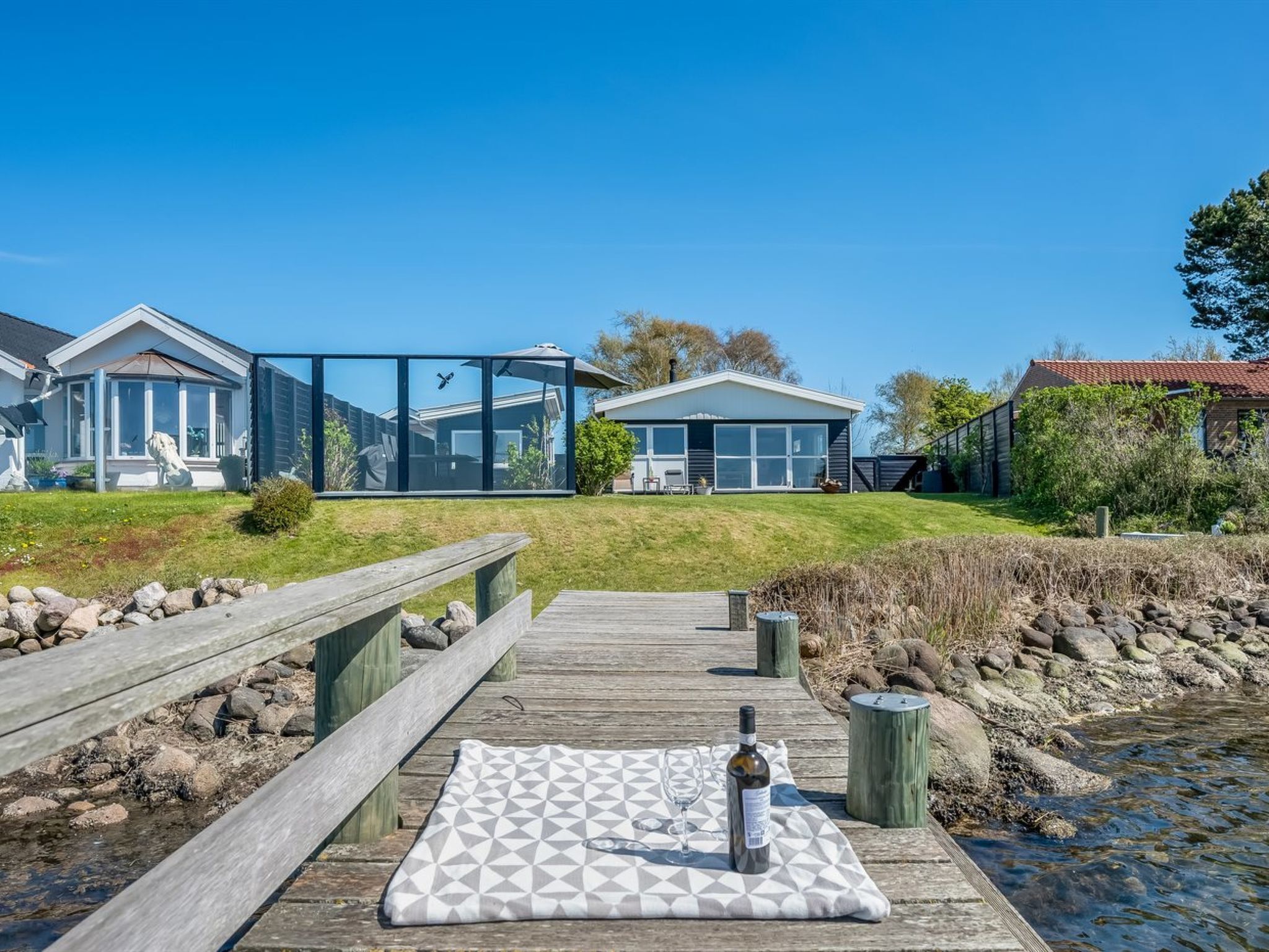 A wooden deck with a picnic setup, a glass house, and a traditional house in the background.