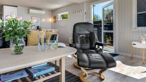 Ein modernes Wohnzimmer mit Ledersessel, Tisch mit Büchern und Blumenvase, und Blick ins Freie.