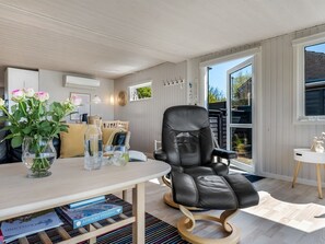 Ein modernes Wohnzimmer mit Ledersessel, Tisch mit Büchern und Blumenvase, und Blick ins Freie.