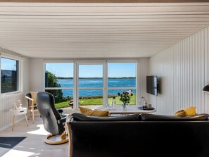 Ein modernes Wohnzimmer mit einem schwarzen Ledersofa, einem kleinen runden Tisch und einem an der Wand befestigten Fernseher.