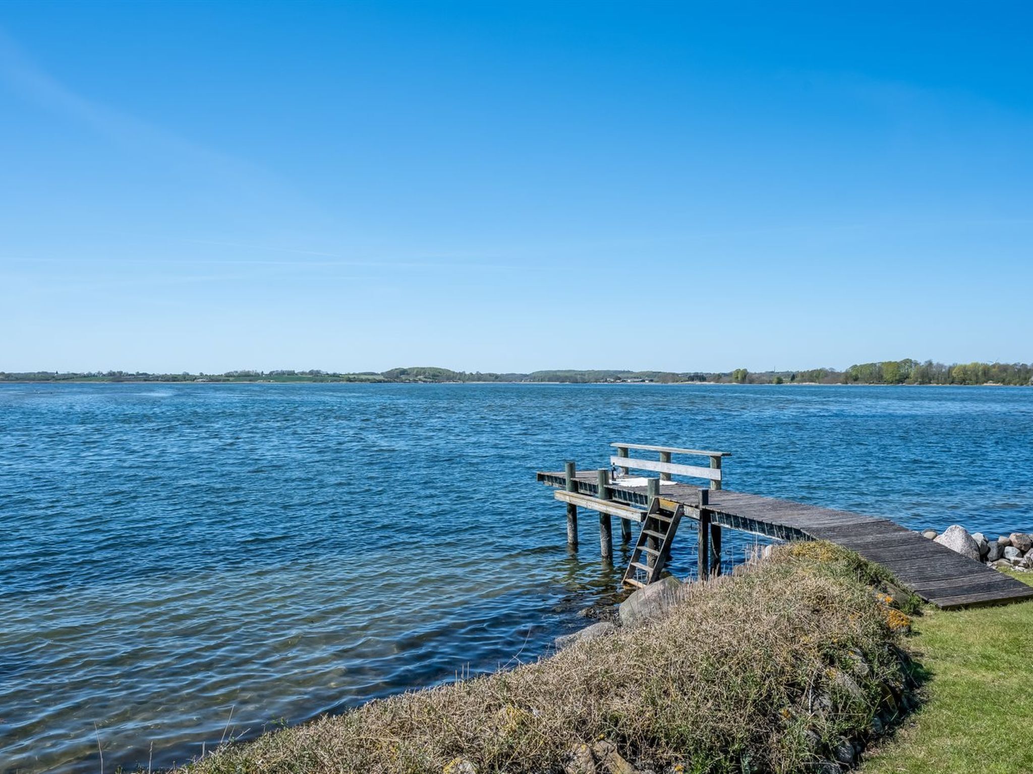 A wooden dock extending into a calm lake with a clear sky.