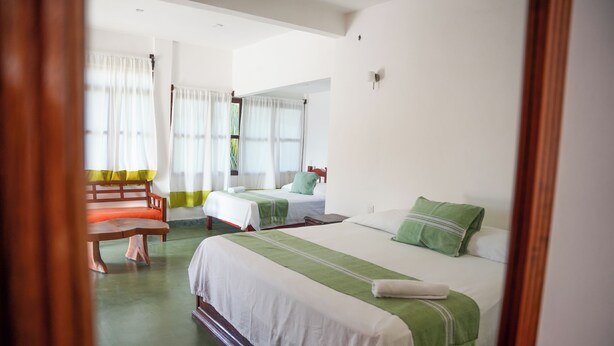 A hotel room with two beds, a wooden bench, and a window with curtains. - Puerta Del Sol (Puerto Escondido)