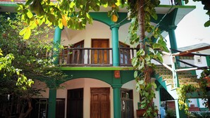 A building with a balcony, wooden doors, and green pillars. - Puerta Del Sol (Puerto Escondido)