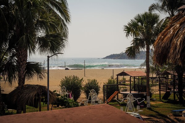 A beach view with palm trees, a sandy beach, and a small structure with a roof. - Puerta Del Sol (Puerto Escondido)