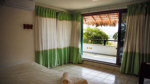 A hotel room with a bed, a window with curtains, a balcony with a view, and a door. - Puerta Del Sol (Puerto Escondido)
