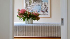En hall med en bänk, en hängande lampa och en inramad målning som föreställer ett kustlandskap.