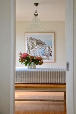 A hallway with a bench, a hanging light fixture, and a framed coastal scene painting. - Mawson House Southern Highlands Views Calm Stylish (Moss Vale)