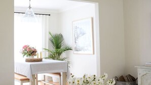 Ett modernt vardagsrum med en vit soffa, ett soffbord med böcker, en vas med blommor, en matplats med bord och stolar samt en öppen spis.