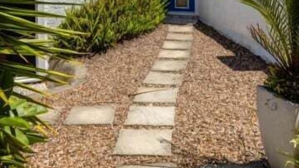 Un bâtiment moderne à l’extérieur blanc, avec une porte bleue et un chemin de pierre menant à l’entrée.