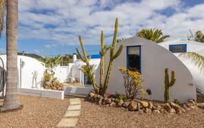 Un bâtiment blanc avec une porte bleue et de nombreux cactus dans le jardin.