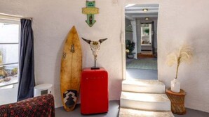 Une pièce avec une planche de surf, une valise rouge, un panneau fixé au mur, un escalier et une plante.