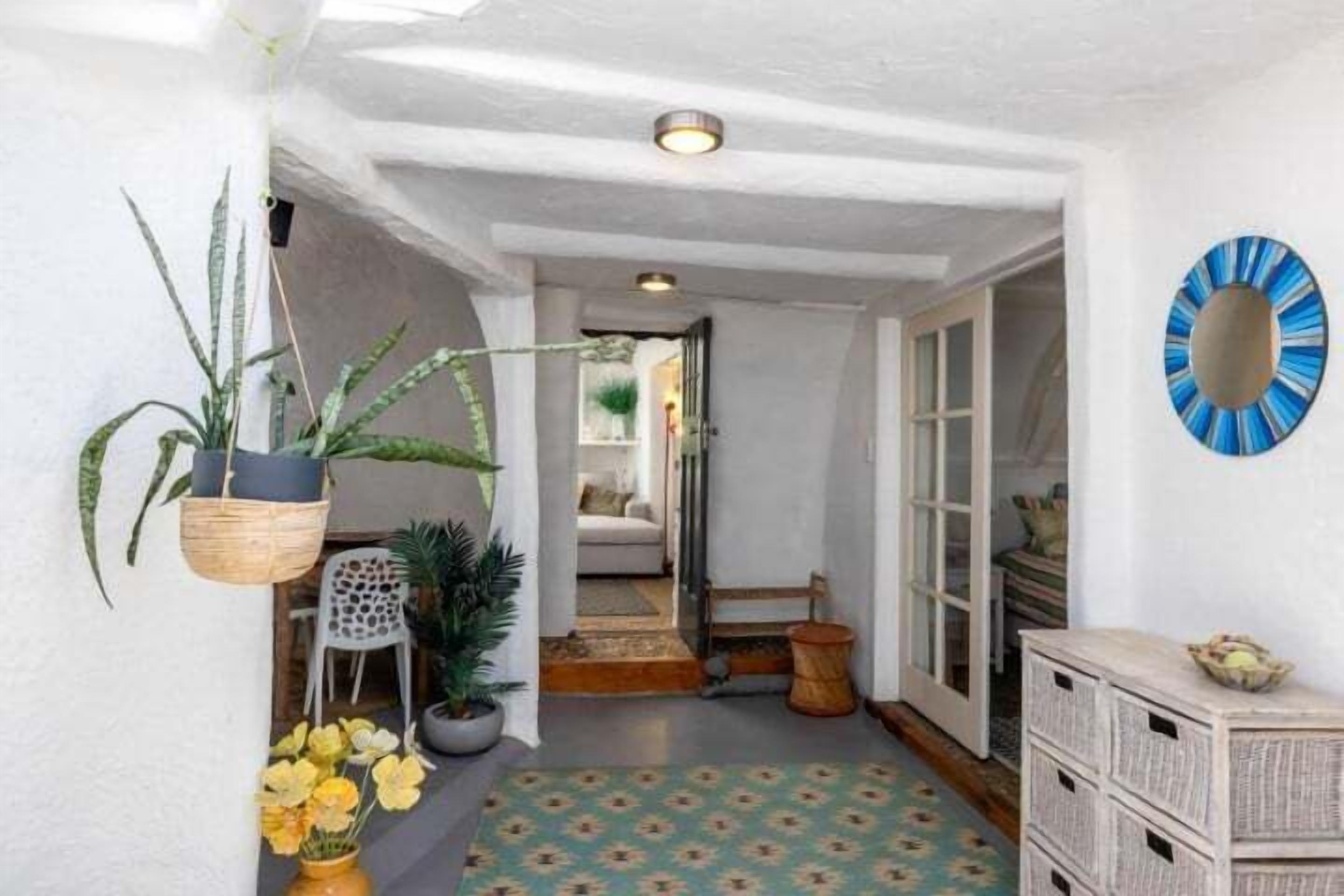 A hallway with a patterned floor, a hanging plant, a wall-mounted mirror, and a wooden chest of drawers.