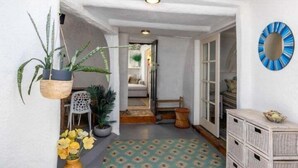 Un couloir avec un sol à motifs, une plante suspendue, un miroir fixé au mur et une commode en bois.