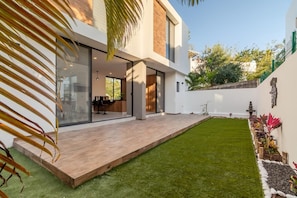 Ein modernes Haus mit Terrasse, Rasen und einem Garten voller Pflanzen.