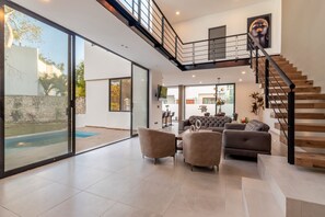 Ein großzügiger Wohnbereich mit einem großen Schiebeglastür, die zu einem Pool führt, einer Treppe mit Holzbalken und einem modernen Interieur.