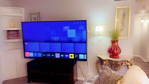 Ein Flachbildfernseher auf einem Standfuß, ein kleiner Tisch mit einer Vase und eine Wand mit einem gerahmten Bild.