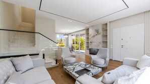 Una sala de estar moderna con una escalera, sofás blancos, una mesa de centro de mármol y un televisor montado en la pared.