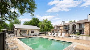 A swimming pool with lounge chairs, a covered seating area, and a building with a stone facade.