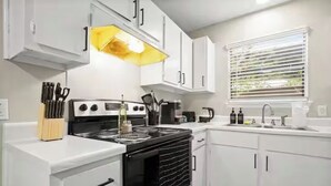 A modern kitchen with white cabinets, a black stove, and a window with blinds.