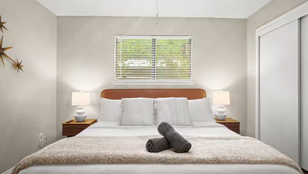A bedroom with a bed, two bedside lamps, a window with blinds, and a star decoration on the wall.