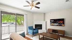 A living room with a sofa, coffee table, TV, fireplace, and a ceiling fan.