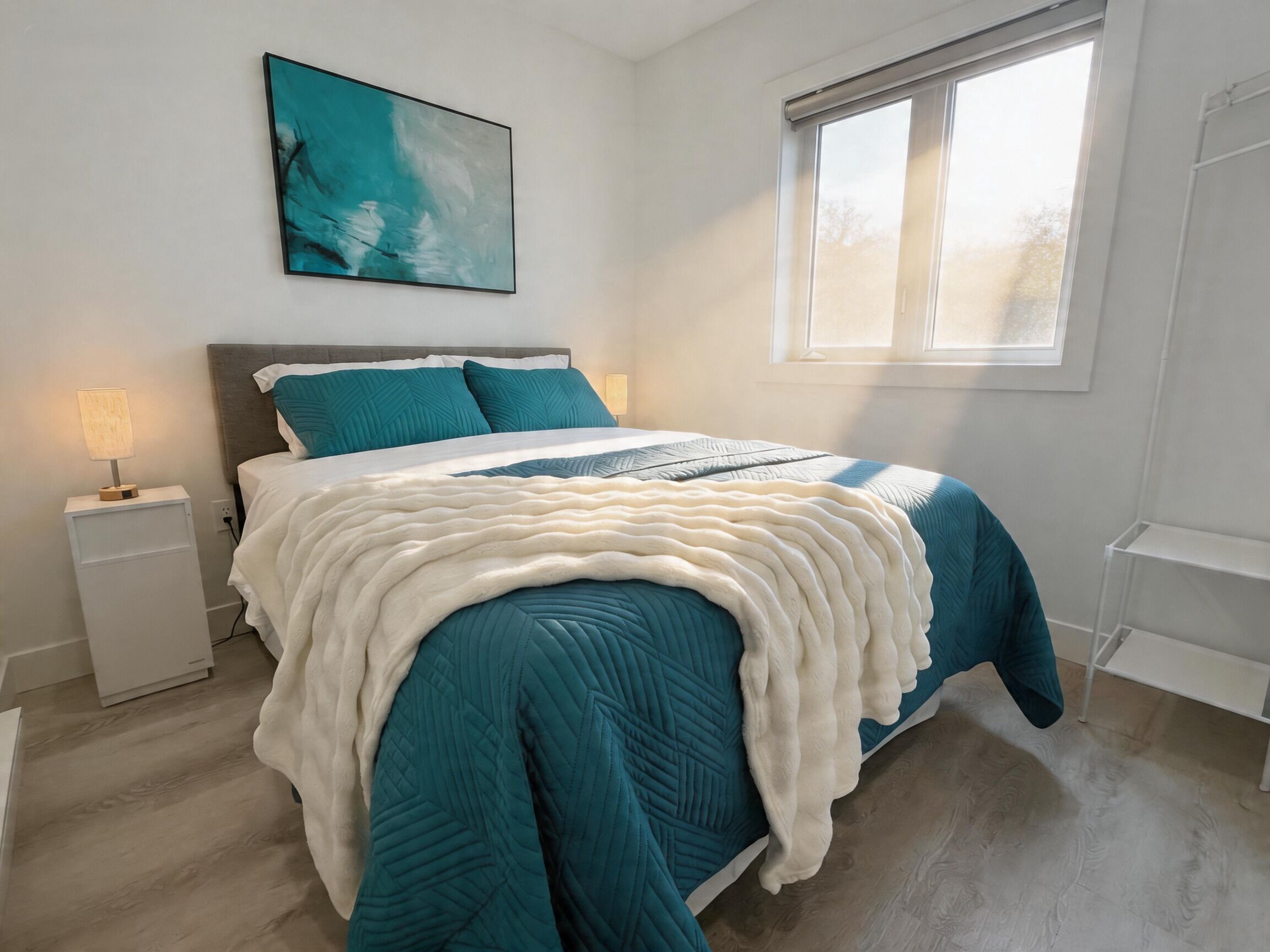 A bedroom with a bed, a nightstand, a lamp, a window, and a painting on the wall.
