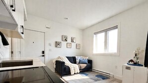 A modern kitchen with a black countertop and cabinets, a dining area with a dark sofa and a white rug, and a window providing natural light. - Vancouver Katherine 2BD 2BA Laneway Home (Vancouver)